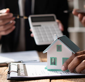 Advisor holding a calculator beside a small model house and a signed document on a clipboard.